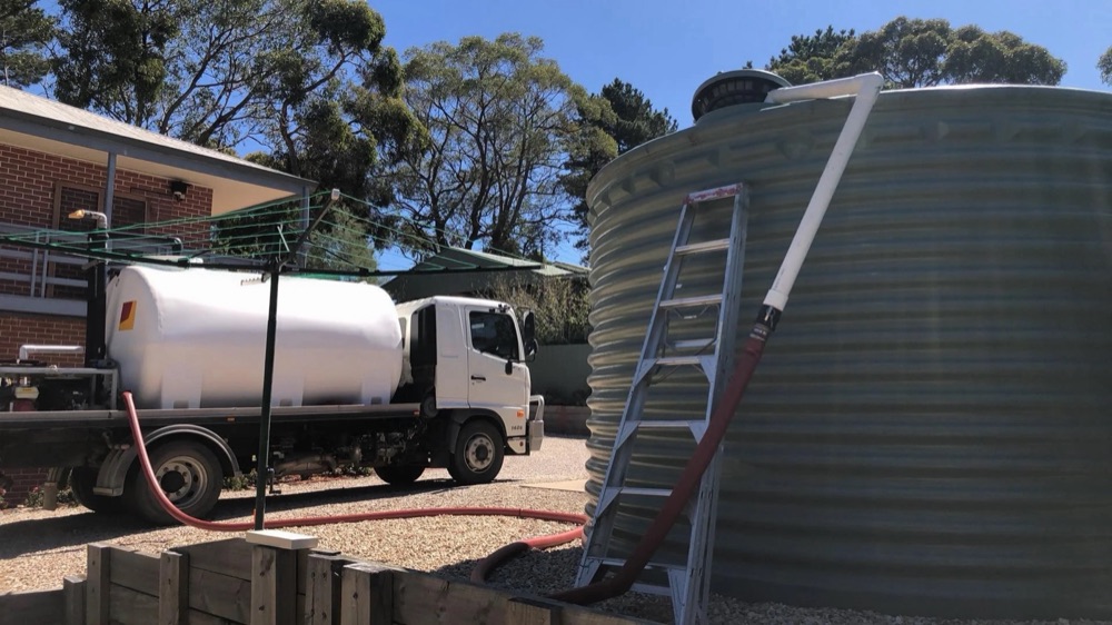 One of your trucks beside a corrugated rainwater tank, the hose run up a ladder into the top